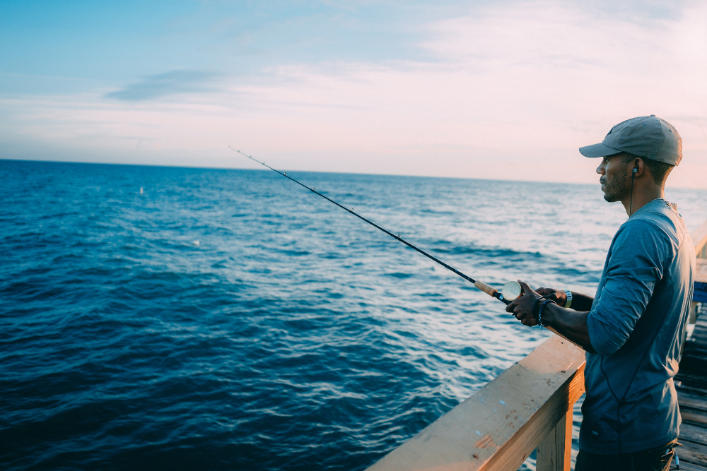 man in hat fishing from pier