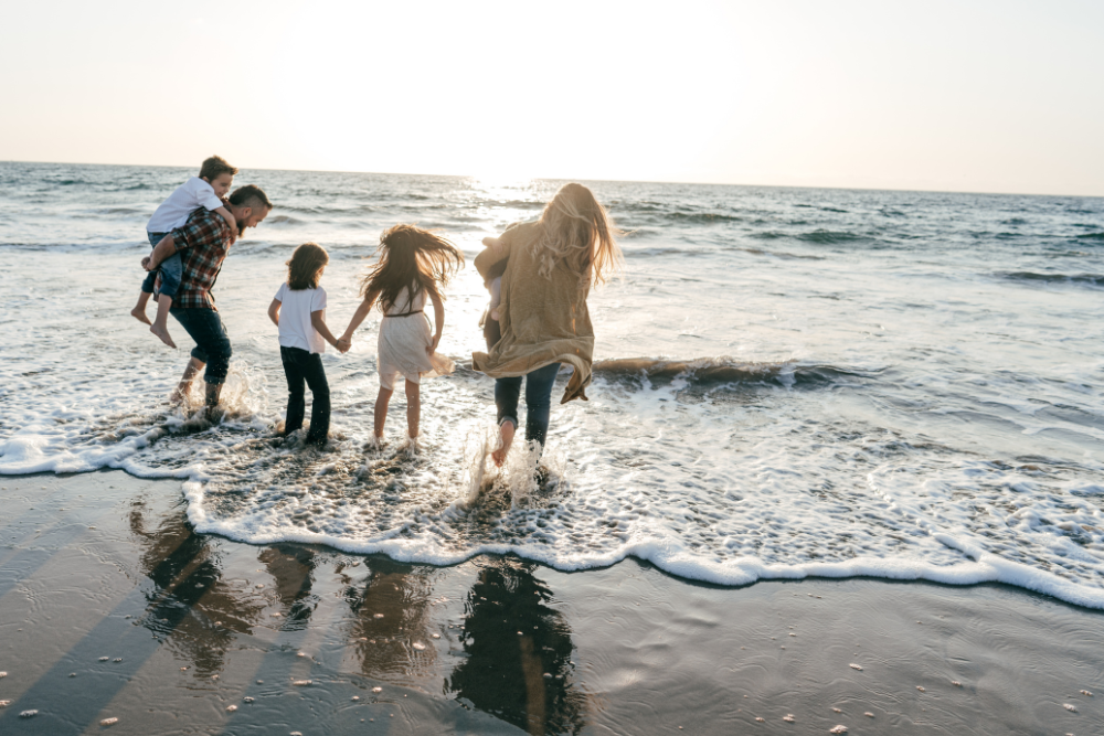 family of five in winter clothes wading in water at the beach